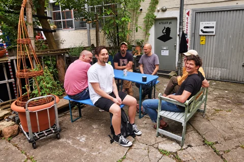 Sechs Teammitglieder sitzen gemeinsam an einem Tisch im begrünten Innenhof.